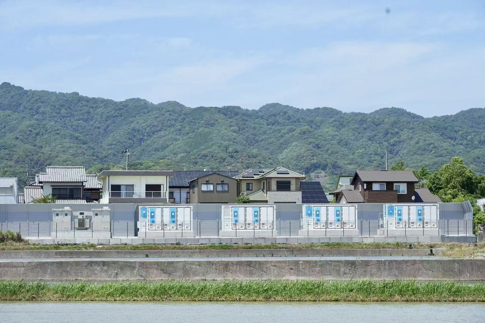 川を挟んだ対岸から見た蓄電所。防音壁の背後に住宅地と山が続く